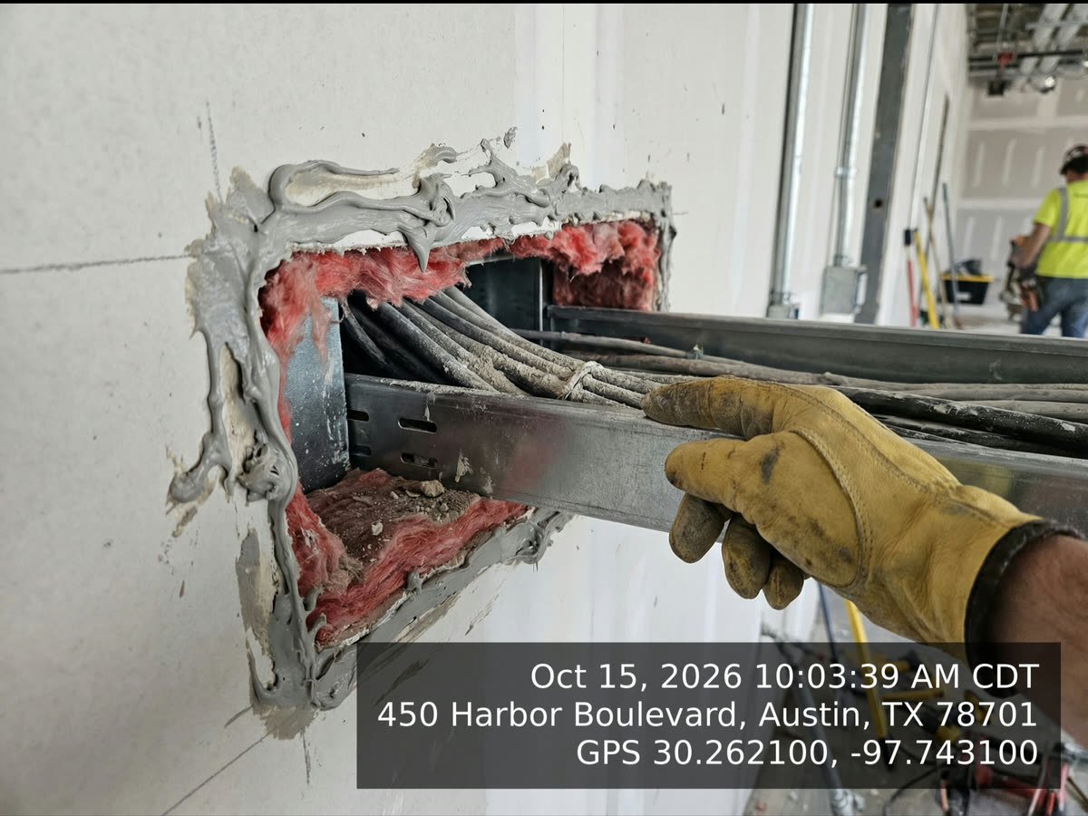 A photo of a cable tray penetration through a wall, stamped in the corner with Oct 15, 2026 10:03:39 AM CDT, a street address in Austin, TX, and GPS coordinates